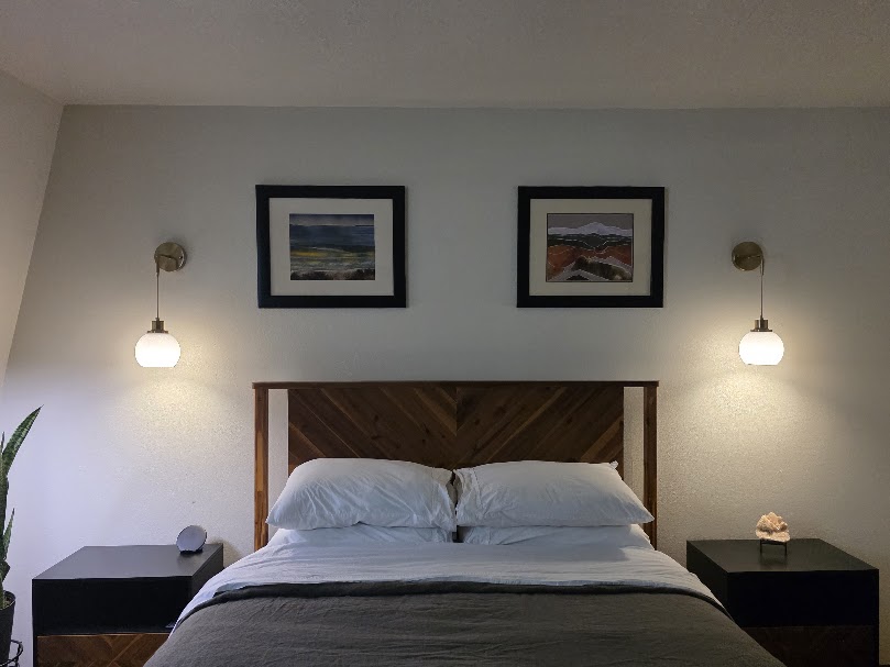 Two original estate sale paintings framed and displayed above a bedroom bed.